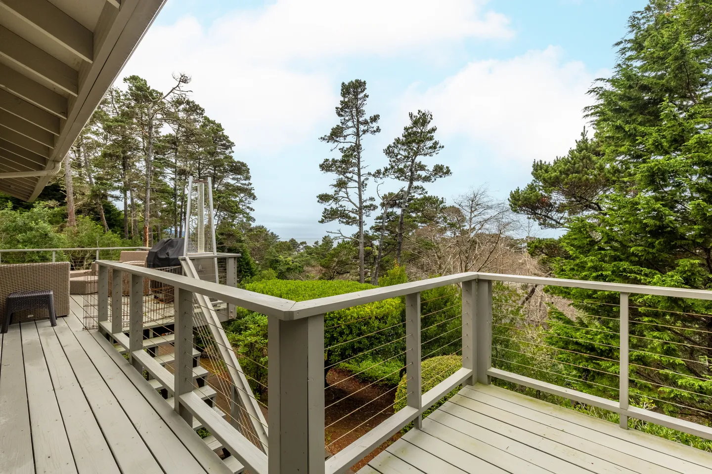 Outdoor elevated deck with painted wood railing, wire cables, and views of surrounding pine trees and foliage.