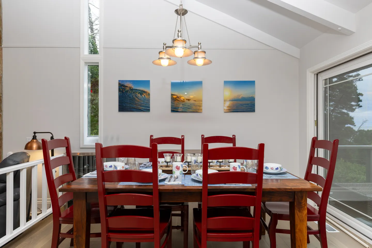 Dining area featuring a wooden table surrounded by red chairs, set for a meal under a three-light chandelier.