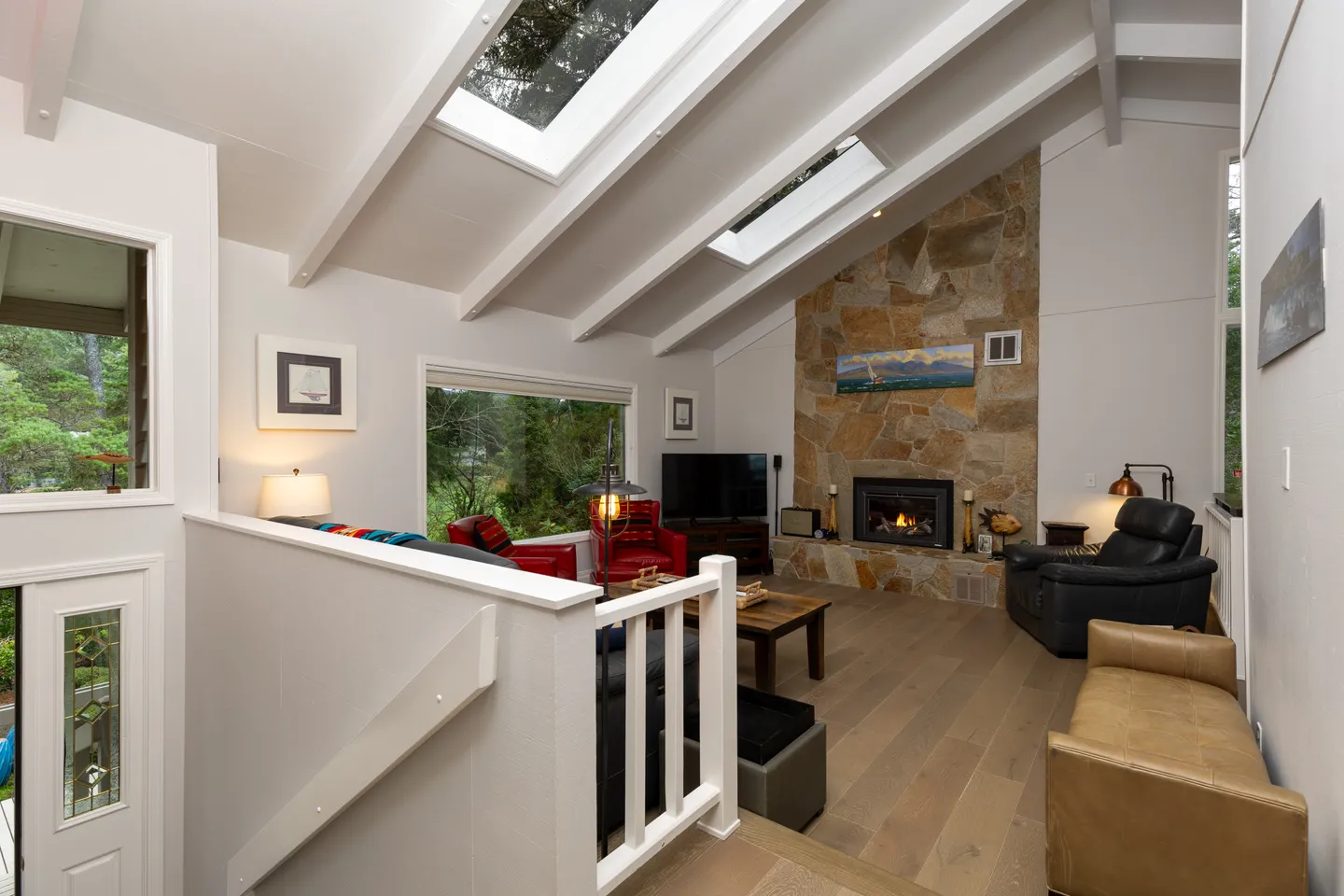 Sunken living room with vaulted exposed-beam ceiling, skylights, stone fireplace, and wood flooring.
