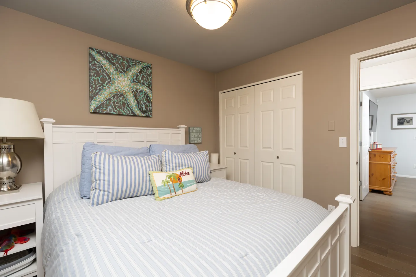 Bedroom featuring a white wooden bed with blue and white striped bedding, a starfish wall print, and closet doors.