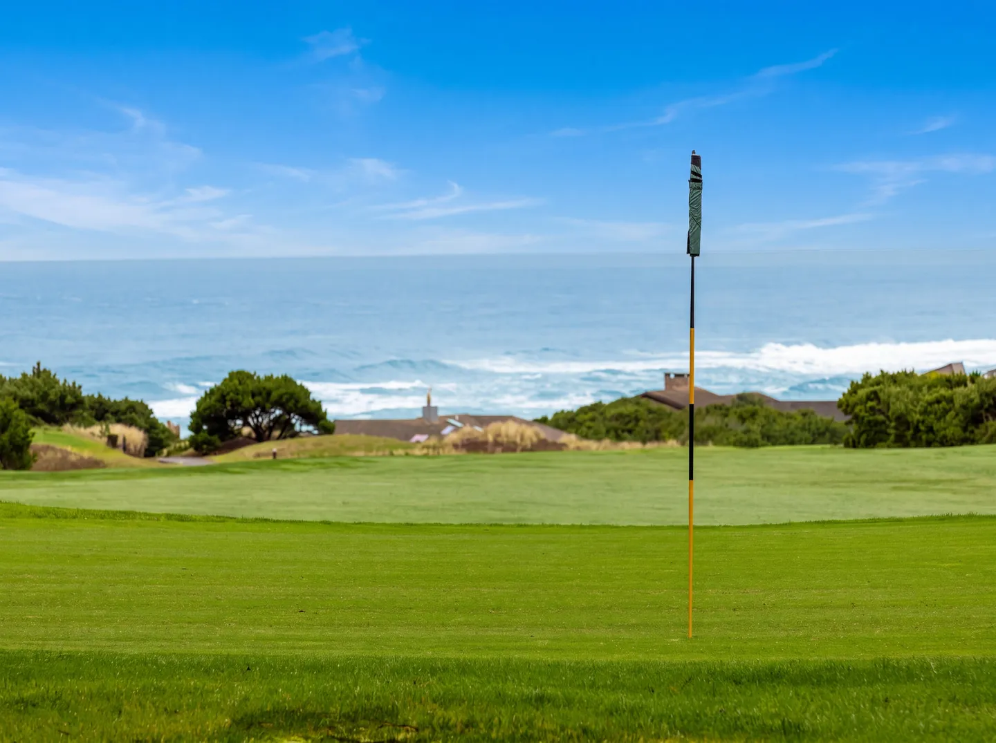 A golf green and flagstick with an expansive ocean view and blue sky in the background.