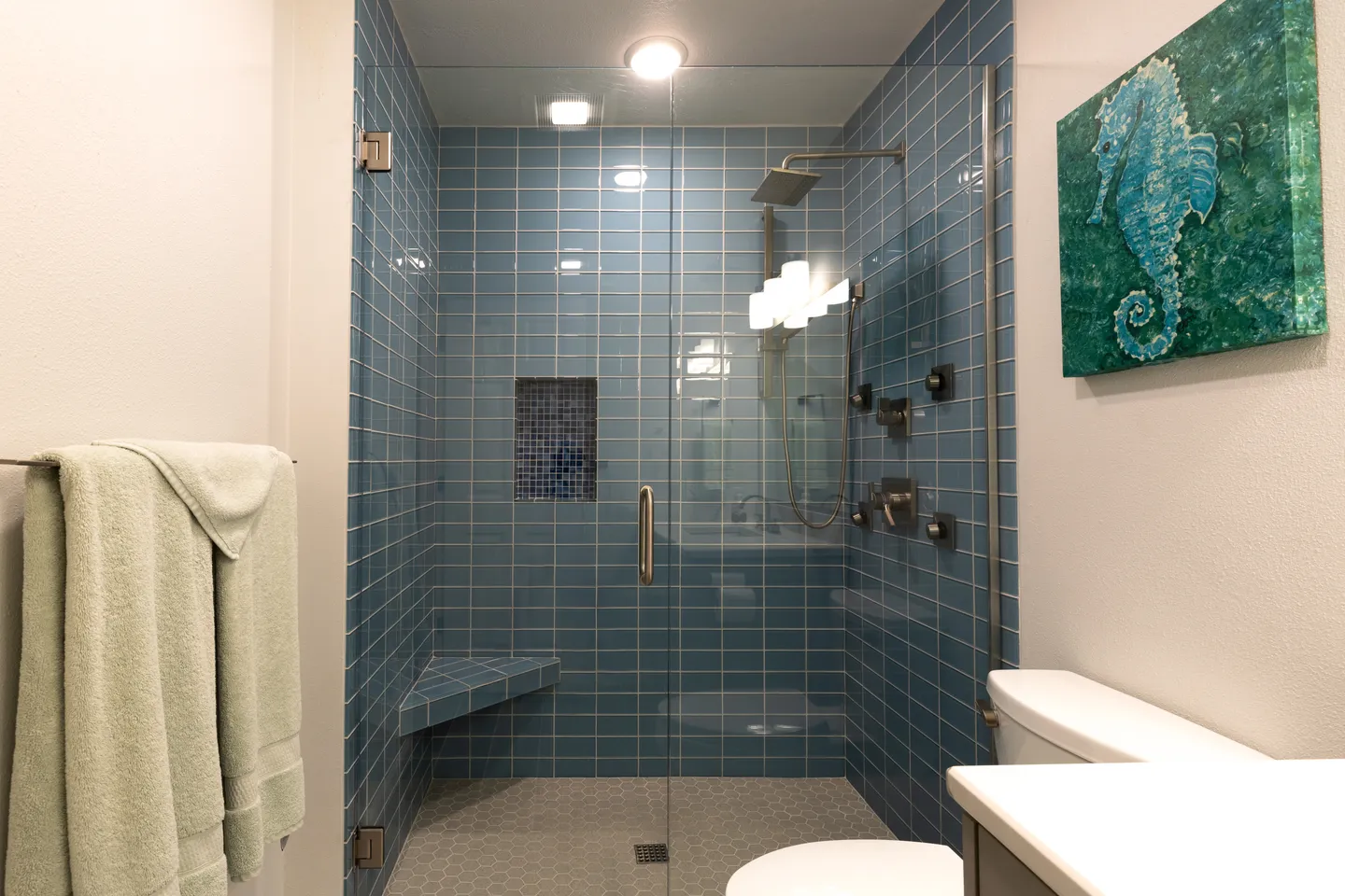 Bathroom with a blue-tiled walk-in shower featuring a glass door, built-in corner bench, and rainfall showerhead.