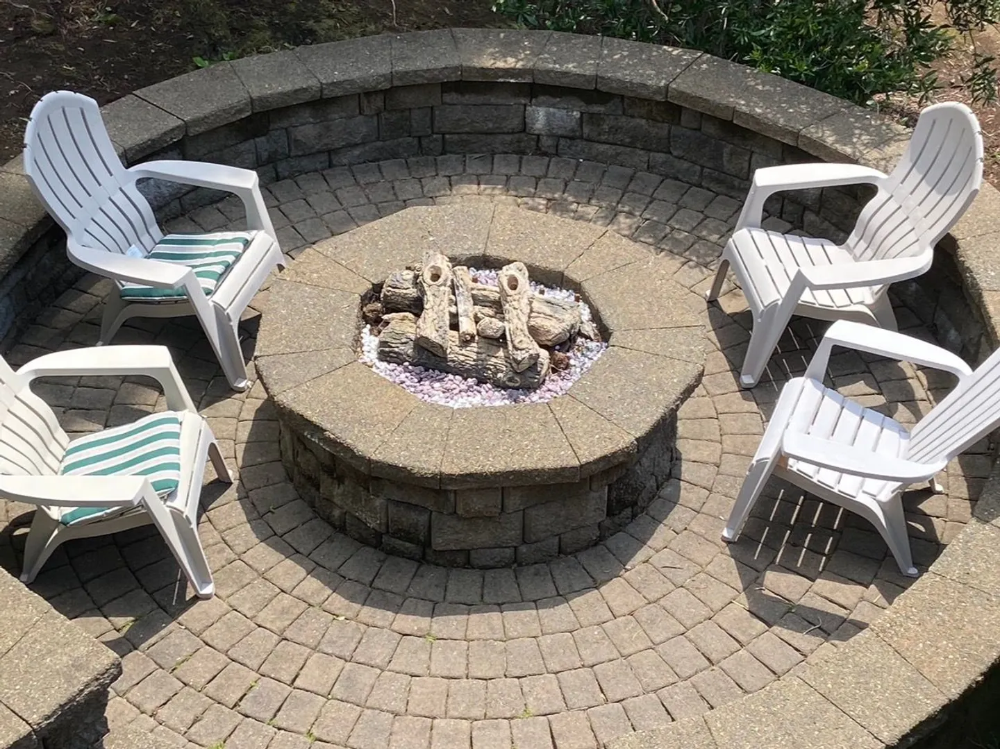 Outdoor circular stone patio featuring a central fire pit surrounded by four white armchairs.