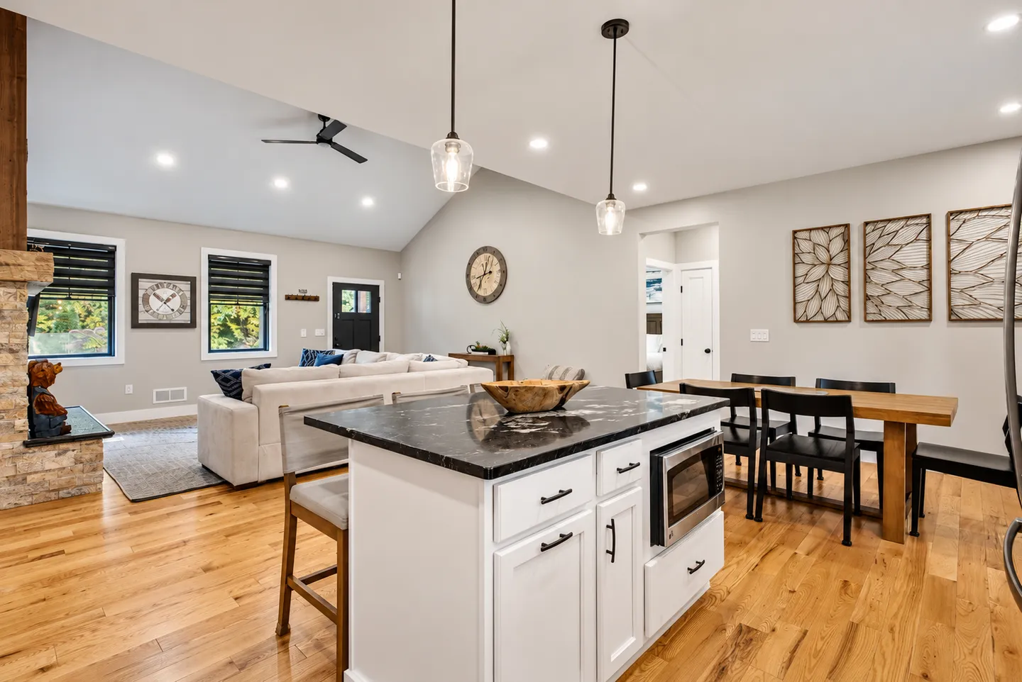 Open-concept living space viewing a kitchen island with dark countertops, dining area, and living room with vaulted ceilings and wood floors.