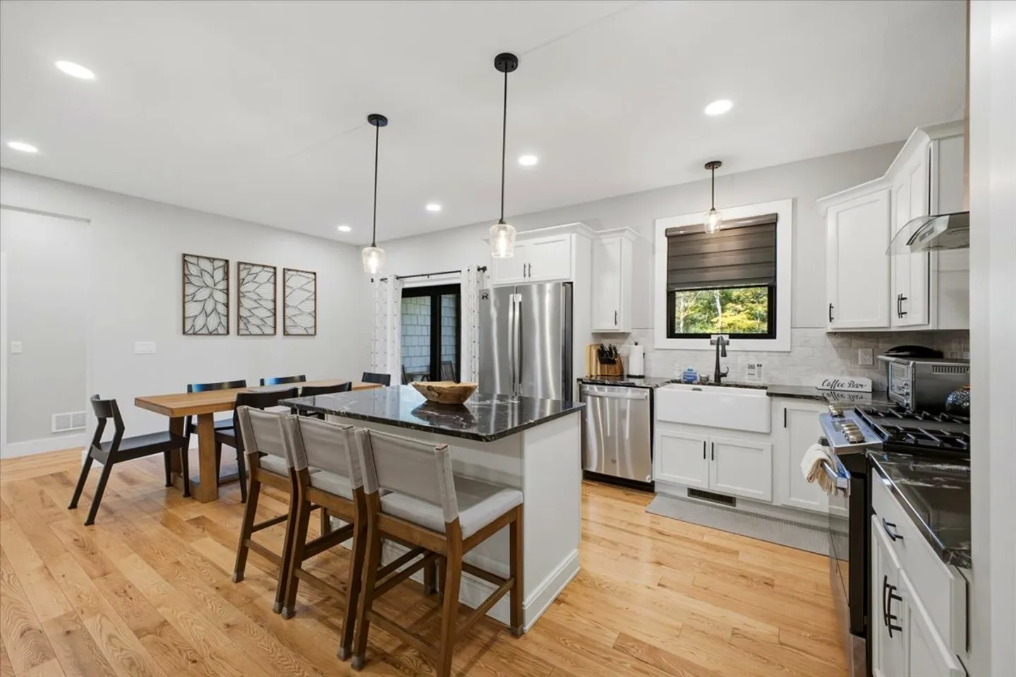 Open-concept kitchen and dining area featuring a kitchen island with barstools, stainless steel appliances, and a wooden dining table.