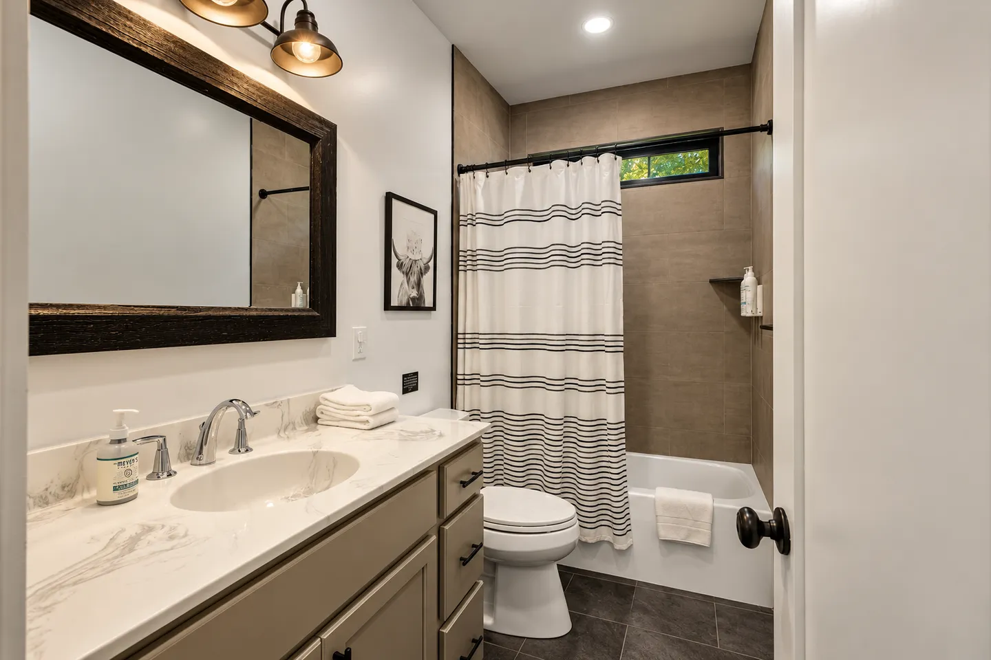 Bathroom featuring a vanity with a dark-framed mirror, a toilet, and a bathtub with a striped shower curtain.