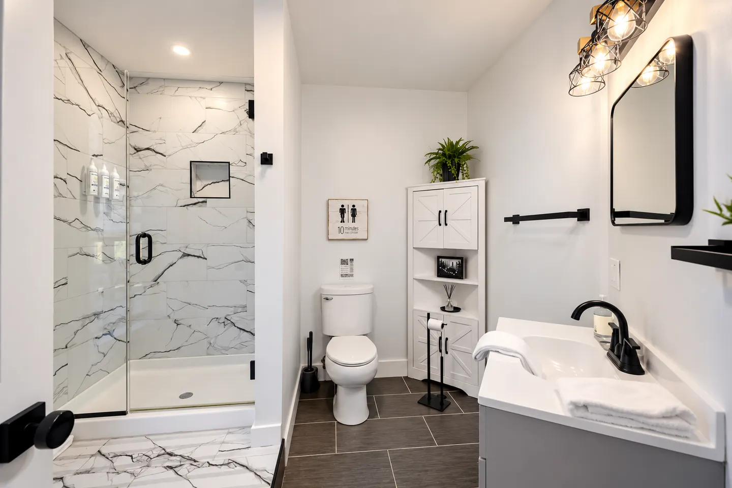 Modern bathroom featuring a walk-in shower with marble-look tile, a white toilet, and a vanity with black hardware.