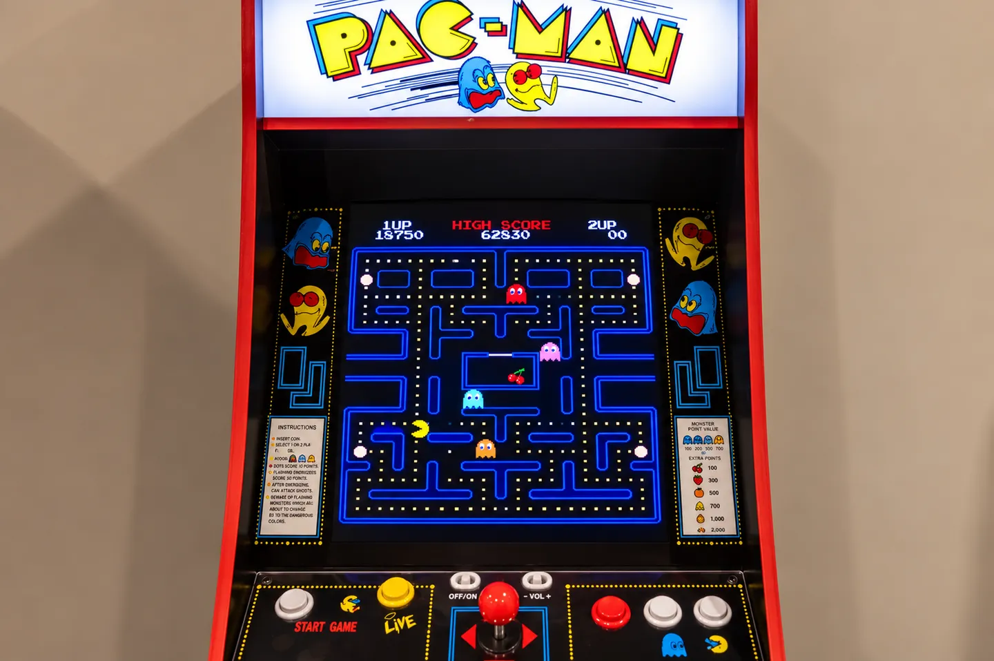 Close-up view of a classic Pac-Man arcade cabinet showing the game screen, marquee, and joystick controls.