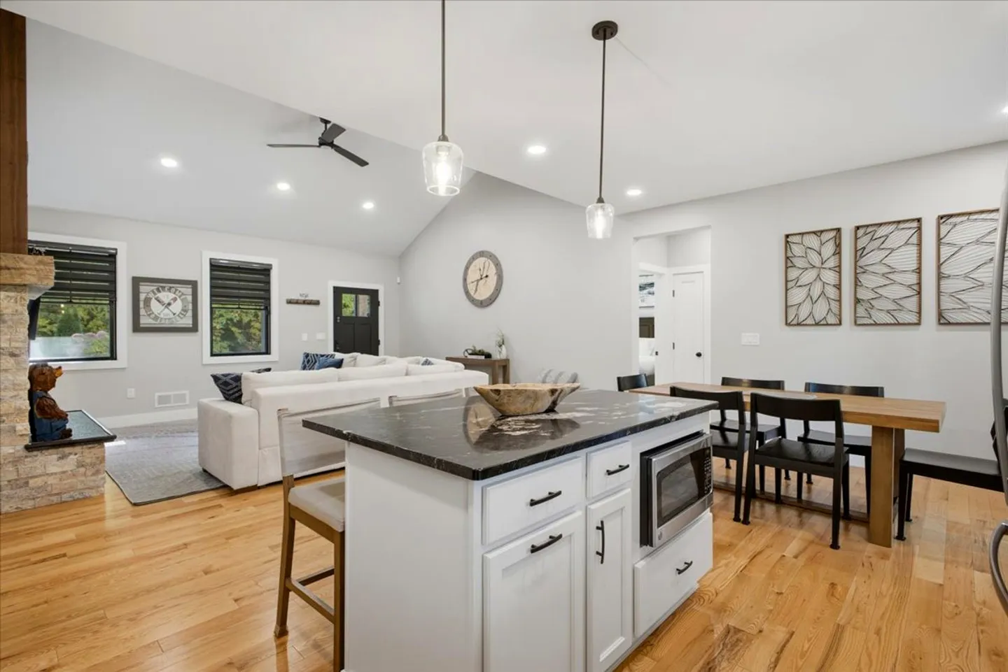 Open-concept living space showing a kitchen island with dark countertop, dining table, and living room with vaulted ceiling.