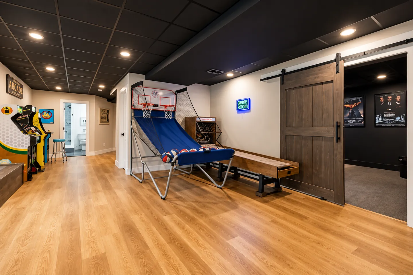 Game room featuring an arcade basketball shootout game, classic arcade cabinets, a shuffleboard table, and an open sliding barn door.