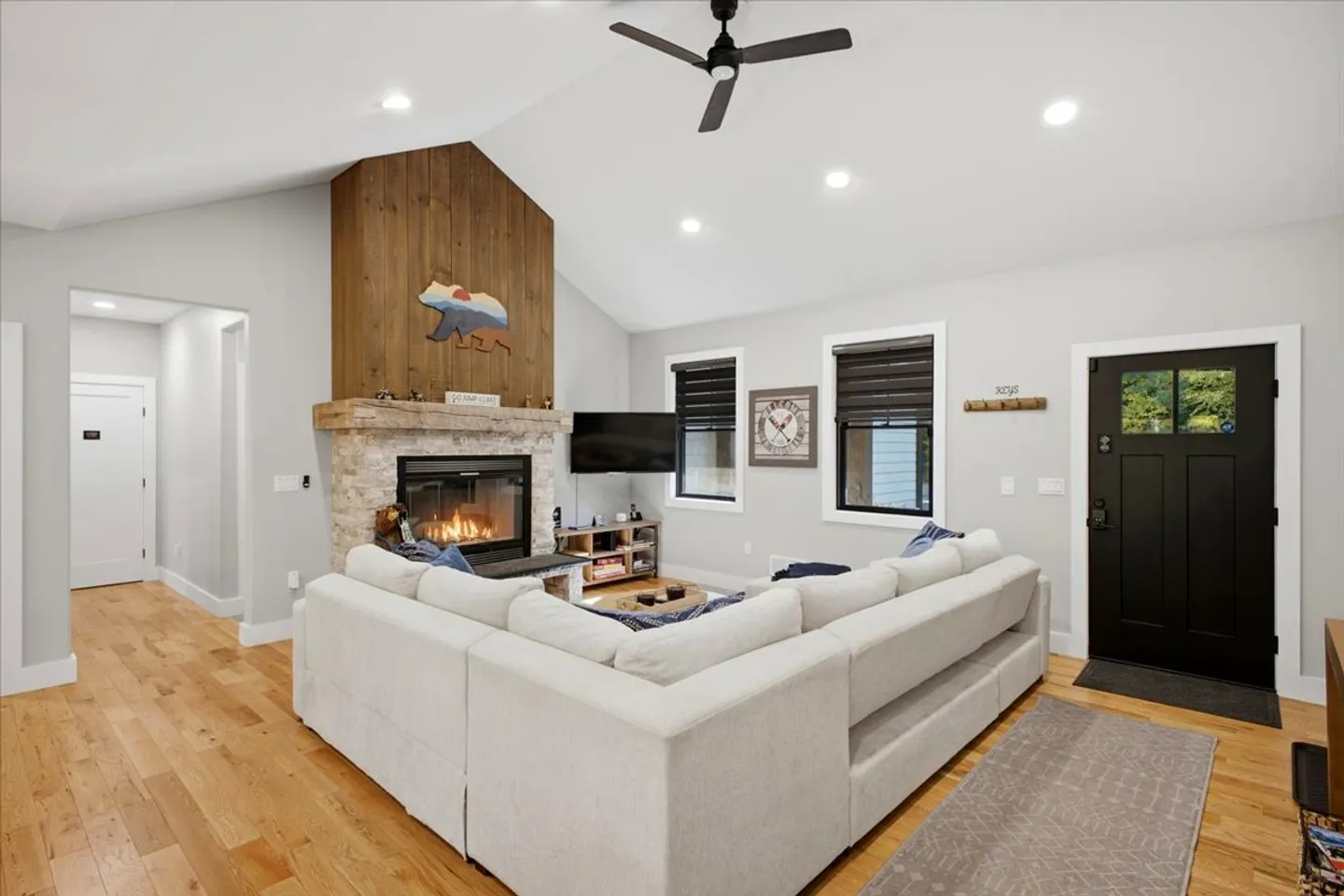 Living room featuring a large sectional sofa, wood-paneled stone fireplace, ceiling fan, and black front door.