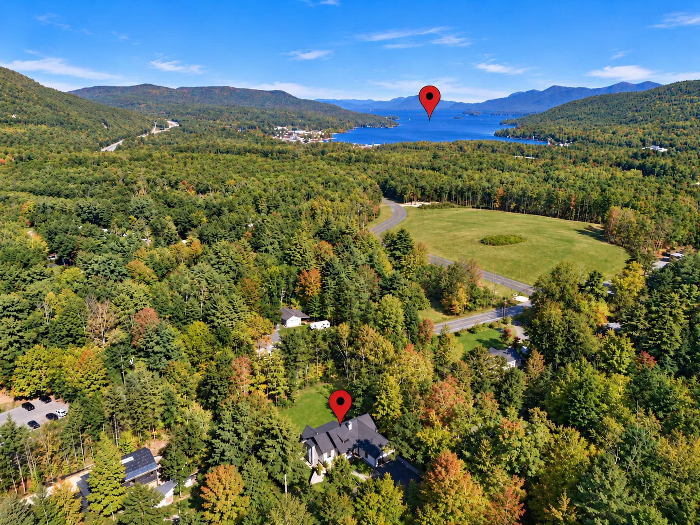 Aerial view showing the property nestled in a dense forest with a large lake and mountains in the background, marked by red location pins.