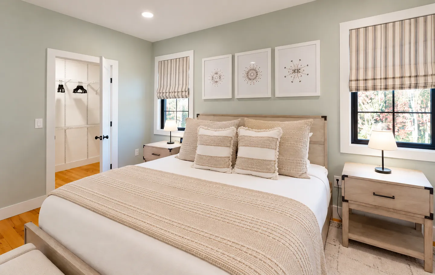 Bedroom with a wooden bed, patterned pillows, matching nightstands with lamps, framed art prints, and an open closet.