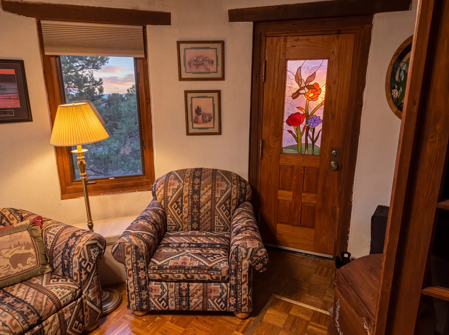 Cozy seating nook featuring patterned armchairs, a floor lamp, a wood door with stained-glass insert, and a window with outdoor views.