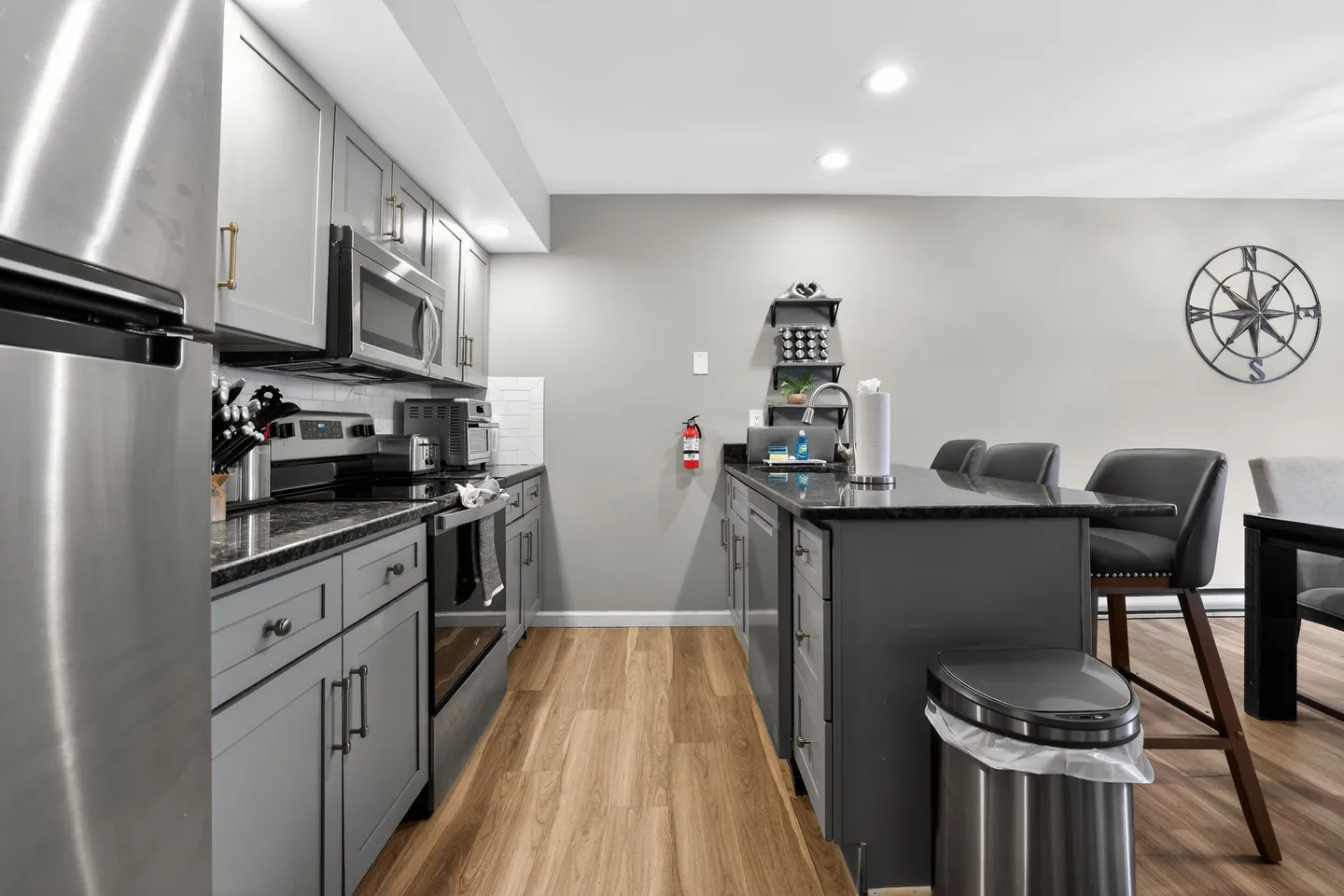 Kitchen with gray cabinetry, dark countertops, stainless steel appliances, and a kitchen island with bar stools.