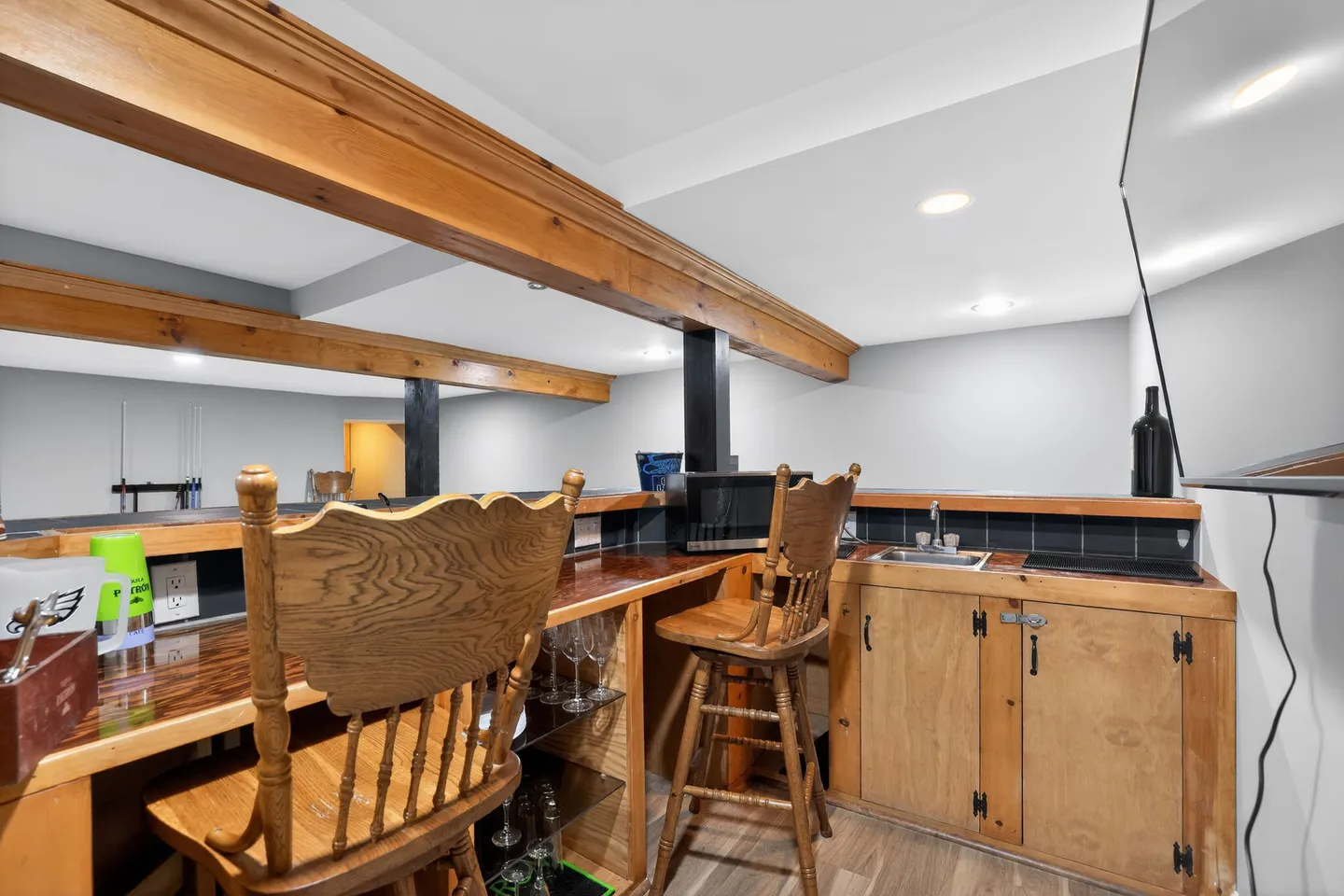 Indoor wet bar featuring wooden cabinetry, bar stools with high backs, a sink, and exposed ceiling beams.