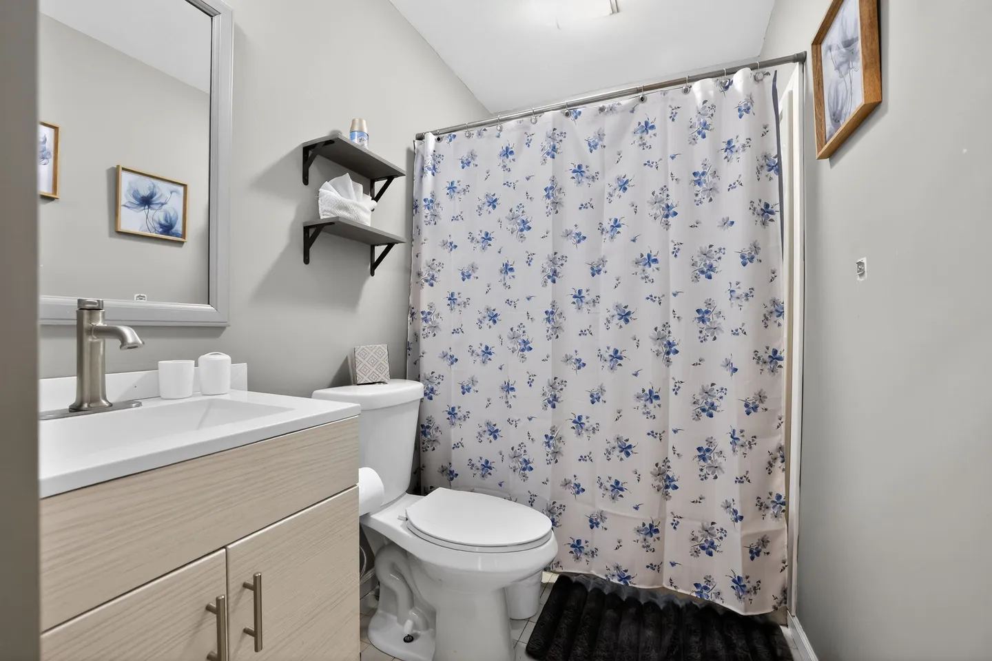 Bathroom featuring a vanity with sink, a toilet, wall-mounted floating shelves, and a shower curtain with a blue floral pattern.