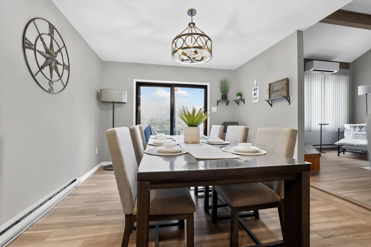 Dining area with a wooden table, upholstered chairs, a hanging chandelier, and sliding glass doors leading outside.