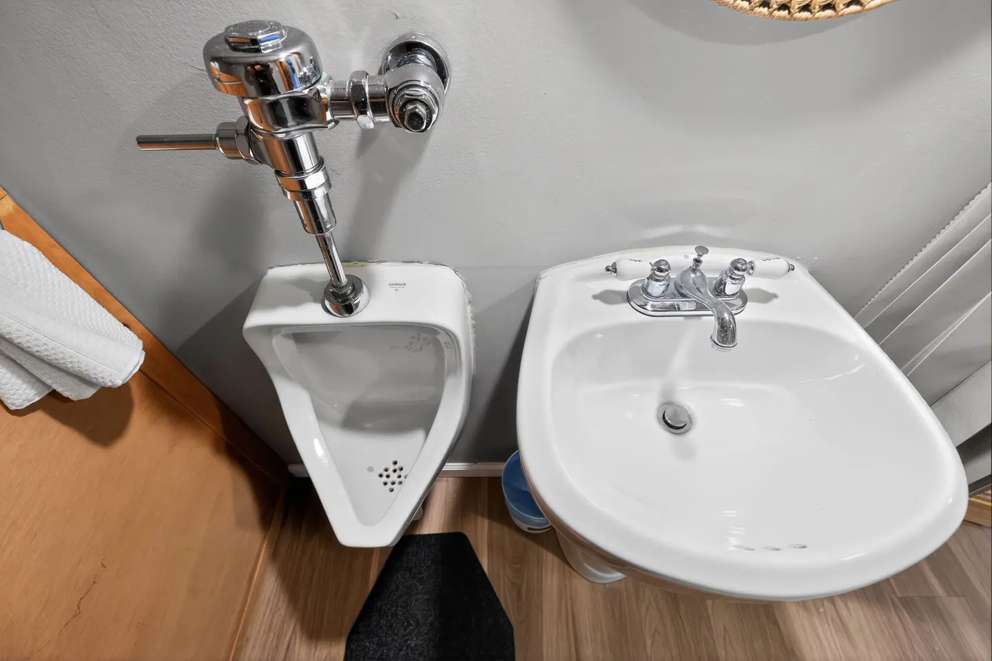 High-angle top-down view of a bathroom showing a wall-mounted urinal alongside a white pedestal sink.
