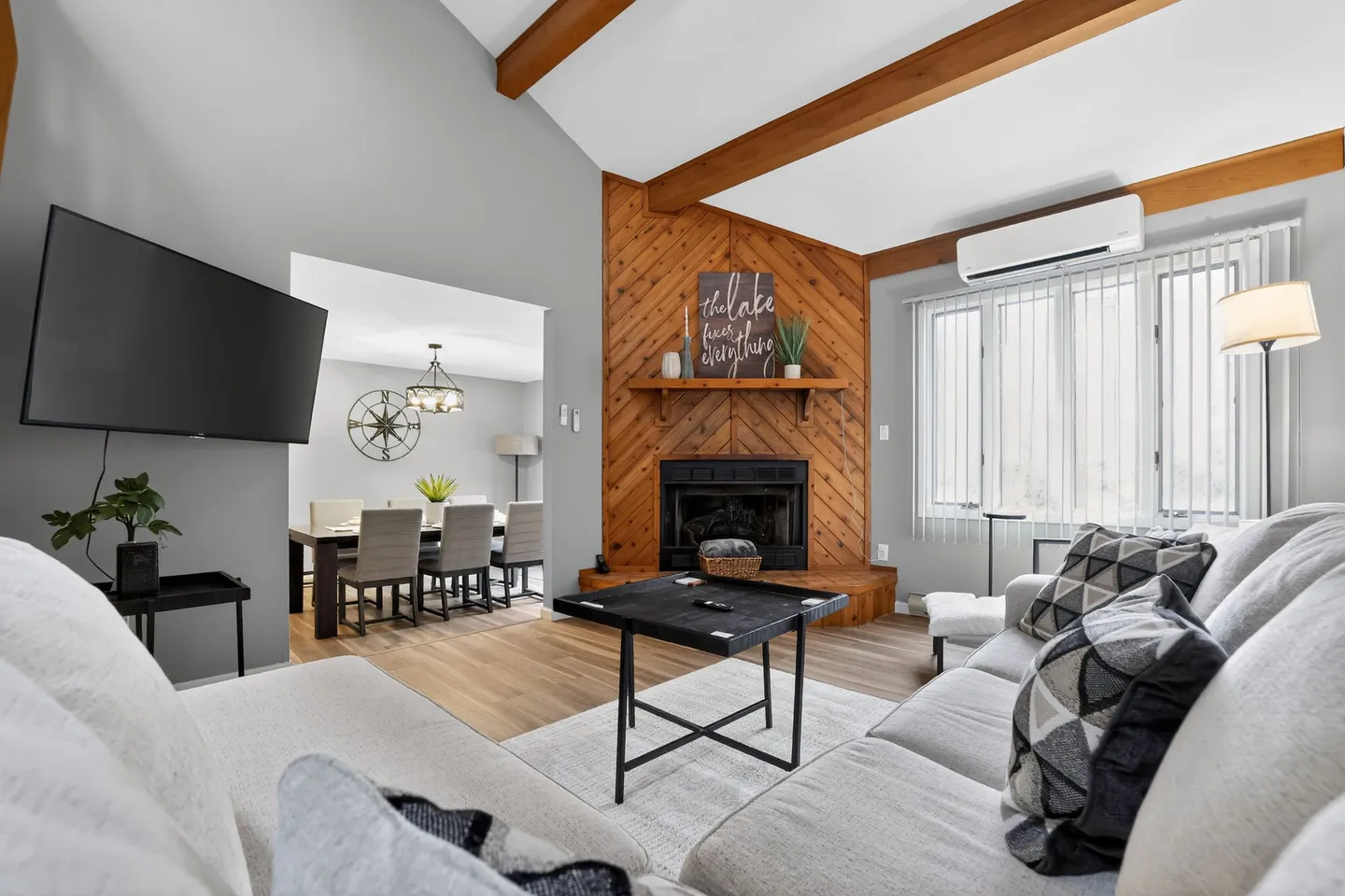 Living room with vaulted wood-beamed ceiling, corner wood-paneled fireplace, sectional couch, and a view into the adjacent dining room.
