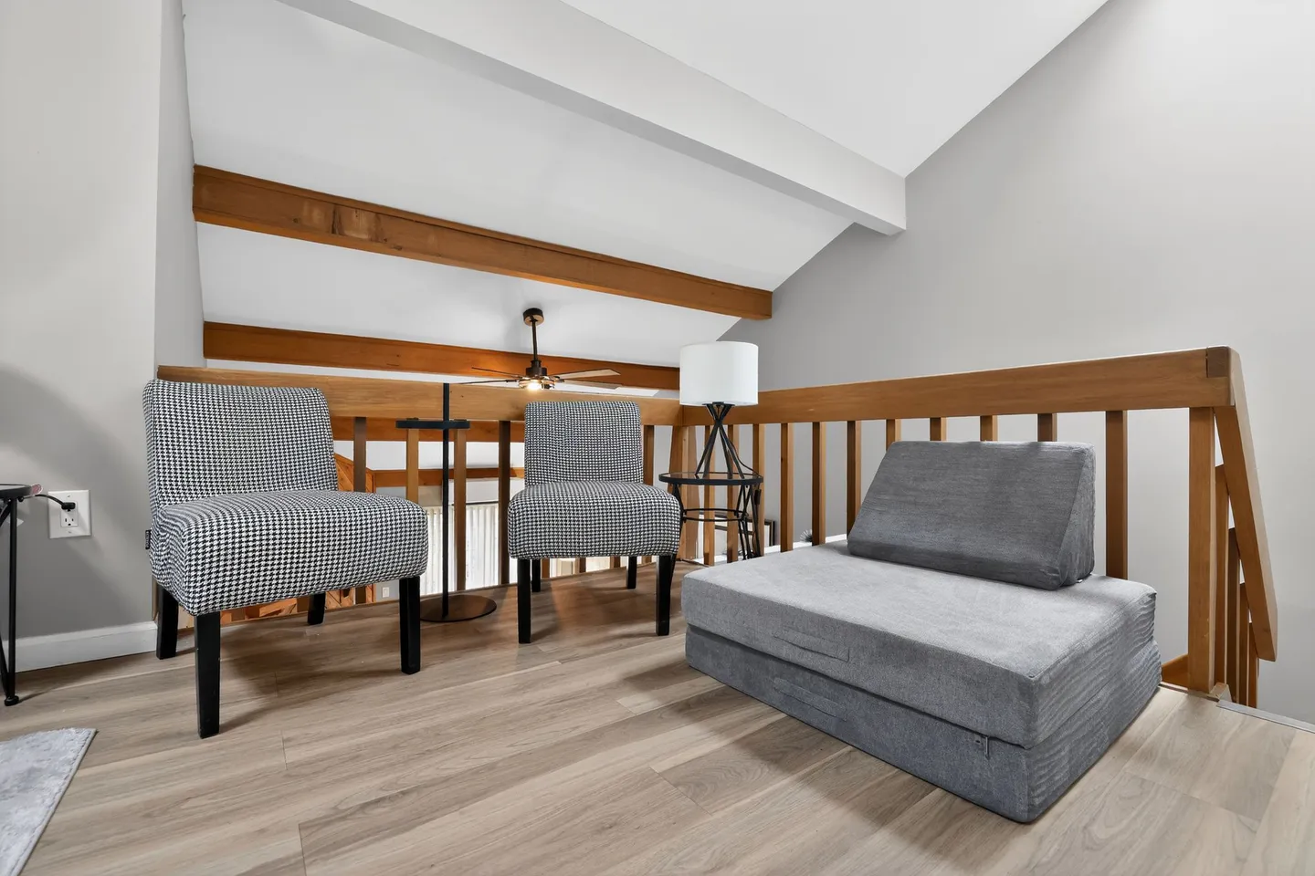 Upstairs loft sitting area with wooden railings, two patterned chairs, and a folding floor mattress.