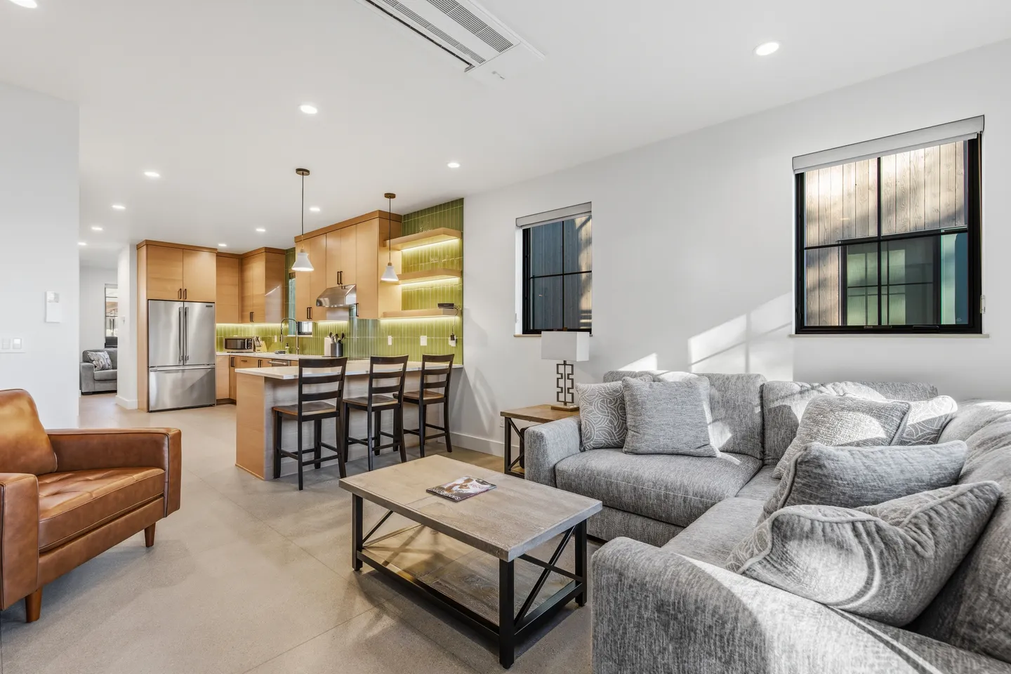 Open-concept living room with a sectional sofa and leather armchair adjacent to a modern kitchen with island seating.