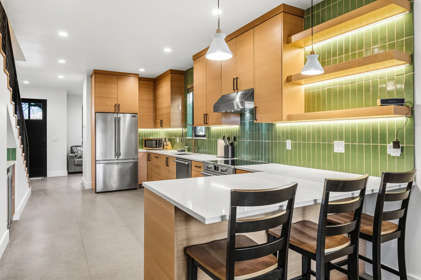 Modern kitchen with light wood cabinetry, green vertical tile backsplash, white countertops, and stainless steel appliances.