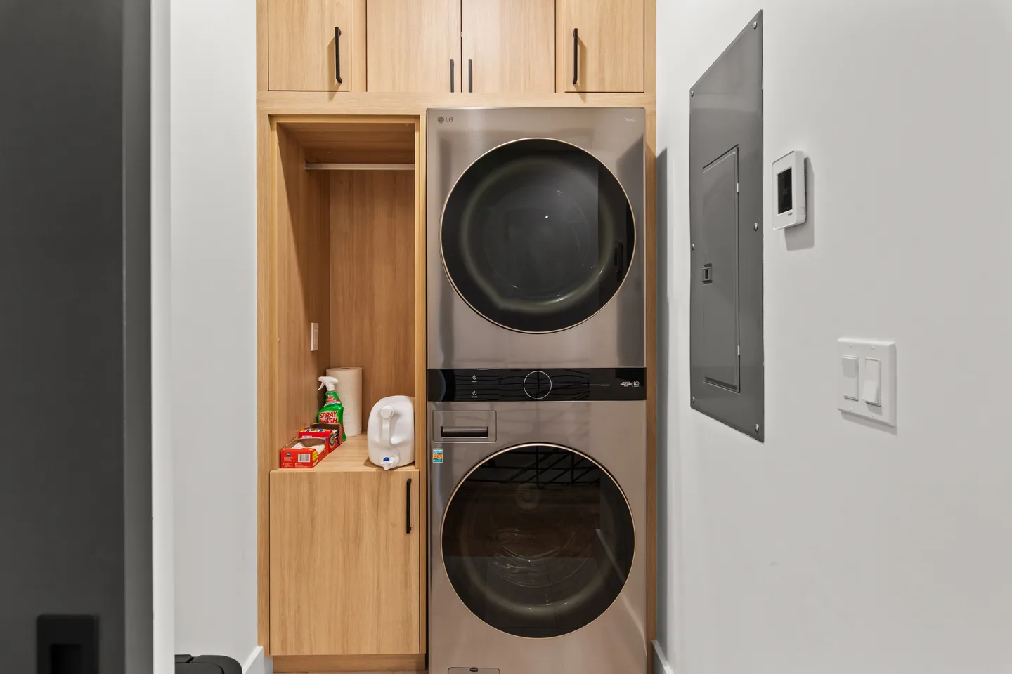 Stackable metallic washer and dryer integrated into light wood cabinetry with built-in storage.