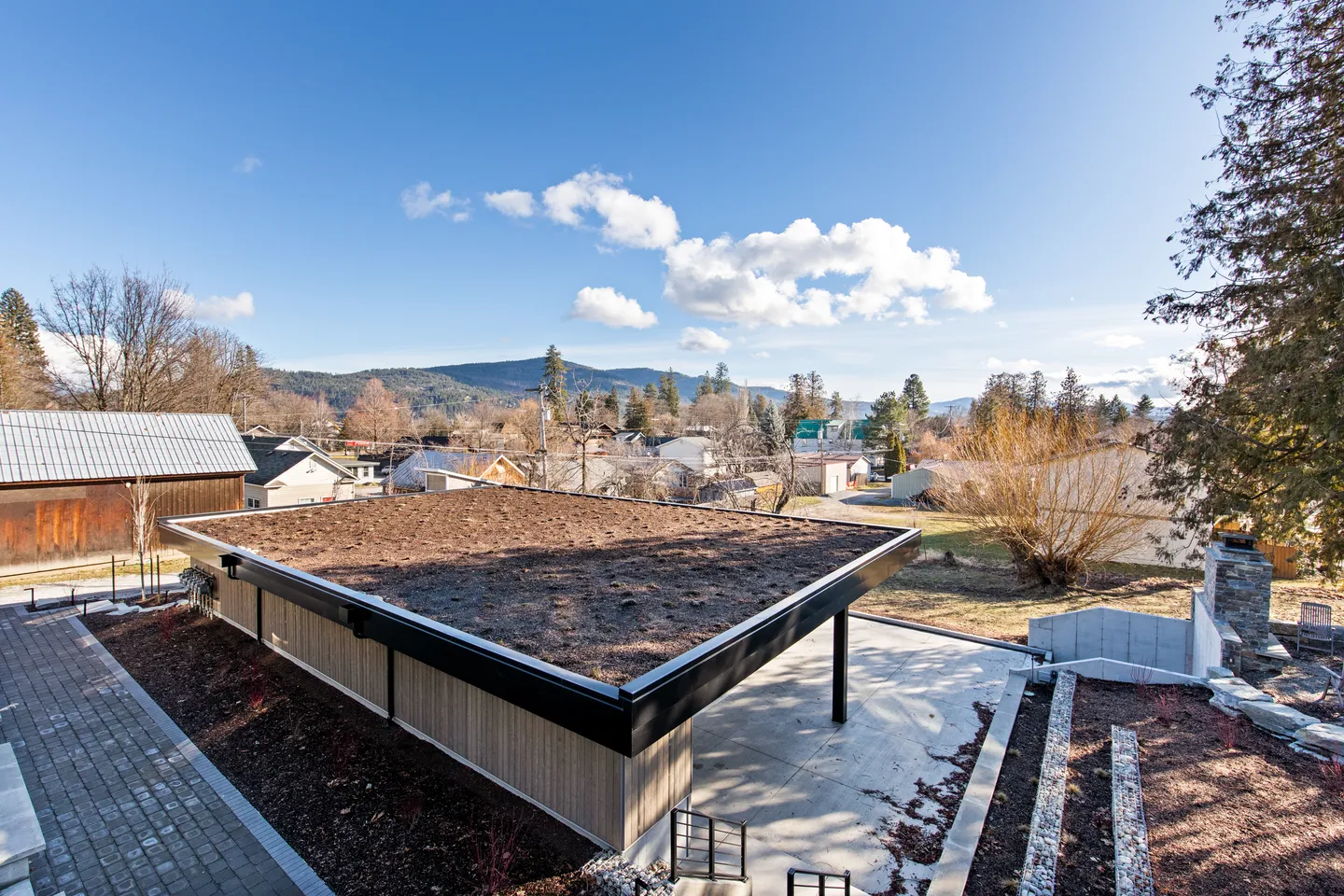 Elevated view of a modern outbuilding featuring a flat green roof and covered patio overlooking a mountain town.