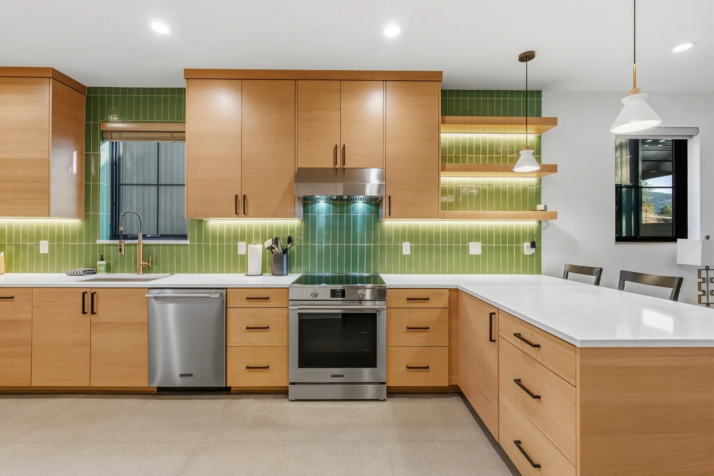Modern kitchen with light wood cabinetry, green vertical tile backsplash, stainless steel appliances, and white countertops.