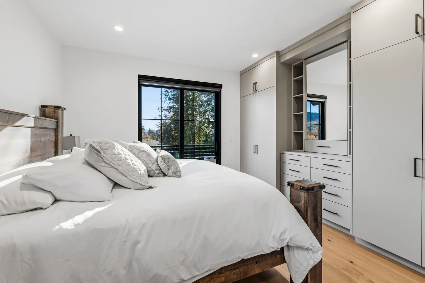 Bedroom with a wooden bed frame, white bedding, built-in storage cabinets, and a glass door leading to a balcony.