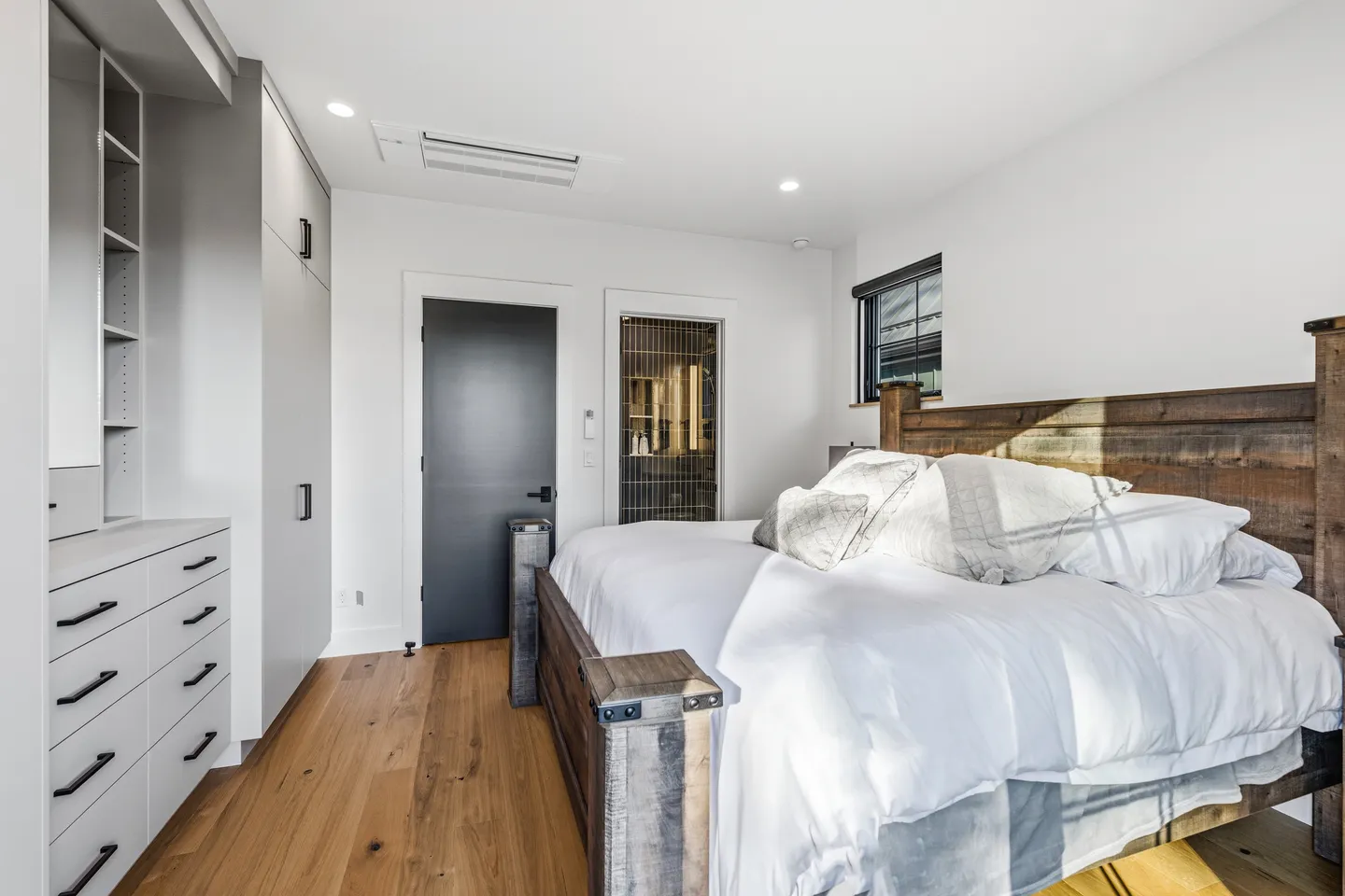 Bedroom featuring a wooden bed frame with white bedding, hardwood floors, built-in gray cabinets, and dark interior doors.