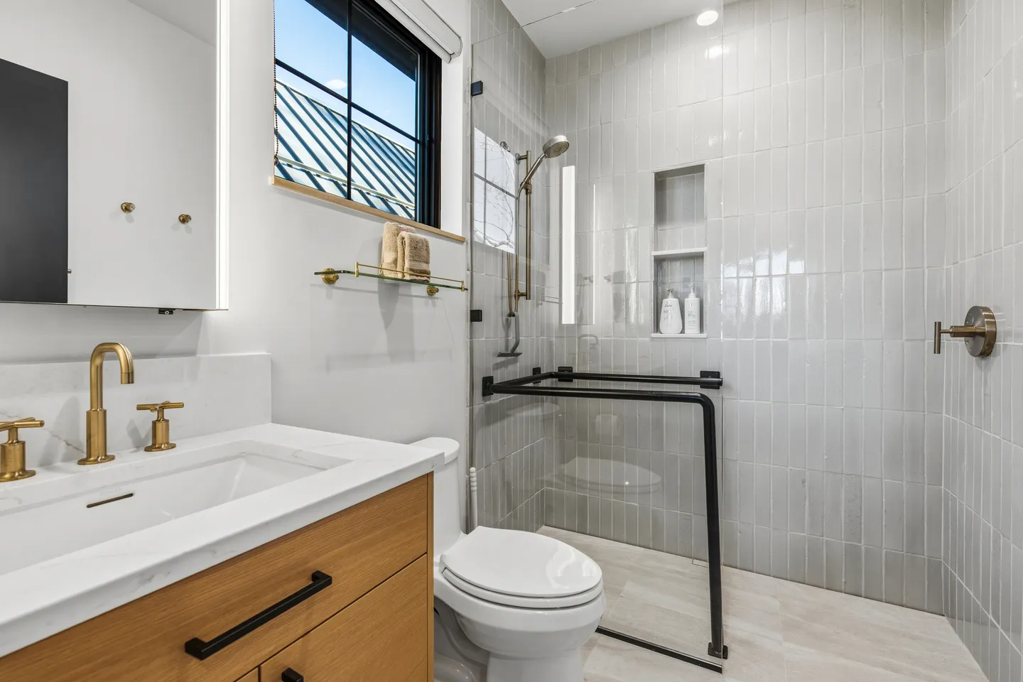 Modern bathroom featuring a wood vanity with gold fixtures, a white toilet, and a glass-enclosed walk-in shower with vertical gray tile.