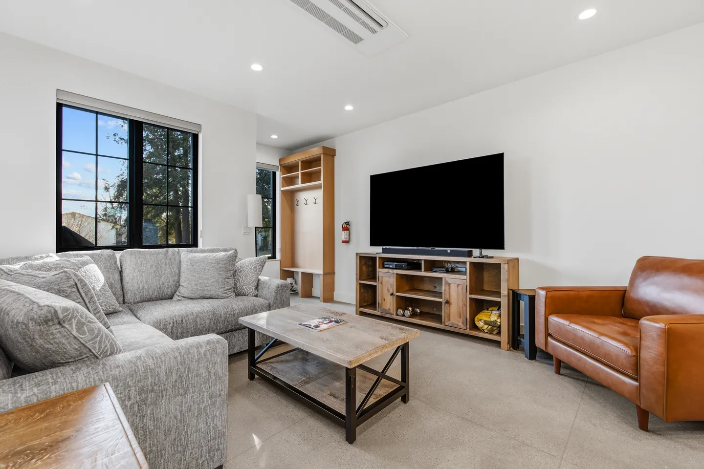 Living room featuring a grey sectional sofa, coffee table, wall-mounted television, wooden media console, and a leather armchair.