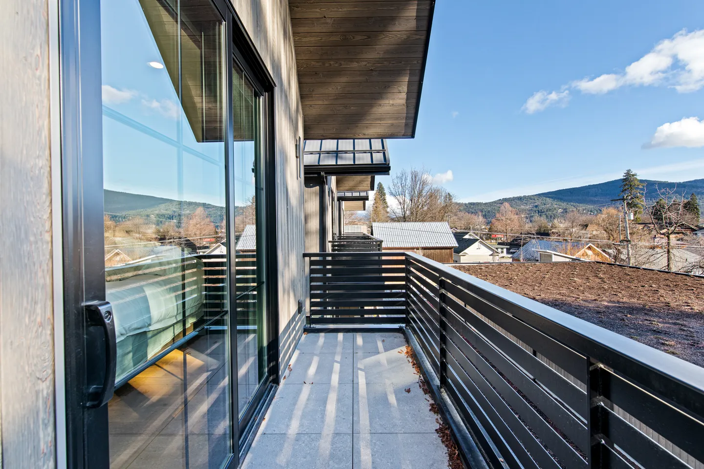 Outdoor balcony with horizontal metal railings, concrete pavers, sliding glass door, and distant mountain views.