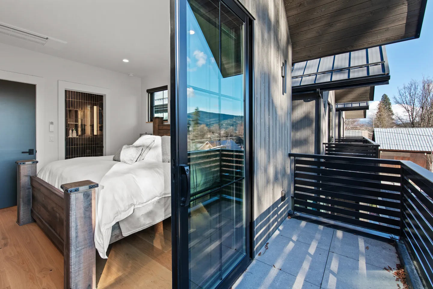 Bedroom with sliding glass door open to a private balcony with black metal railings.