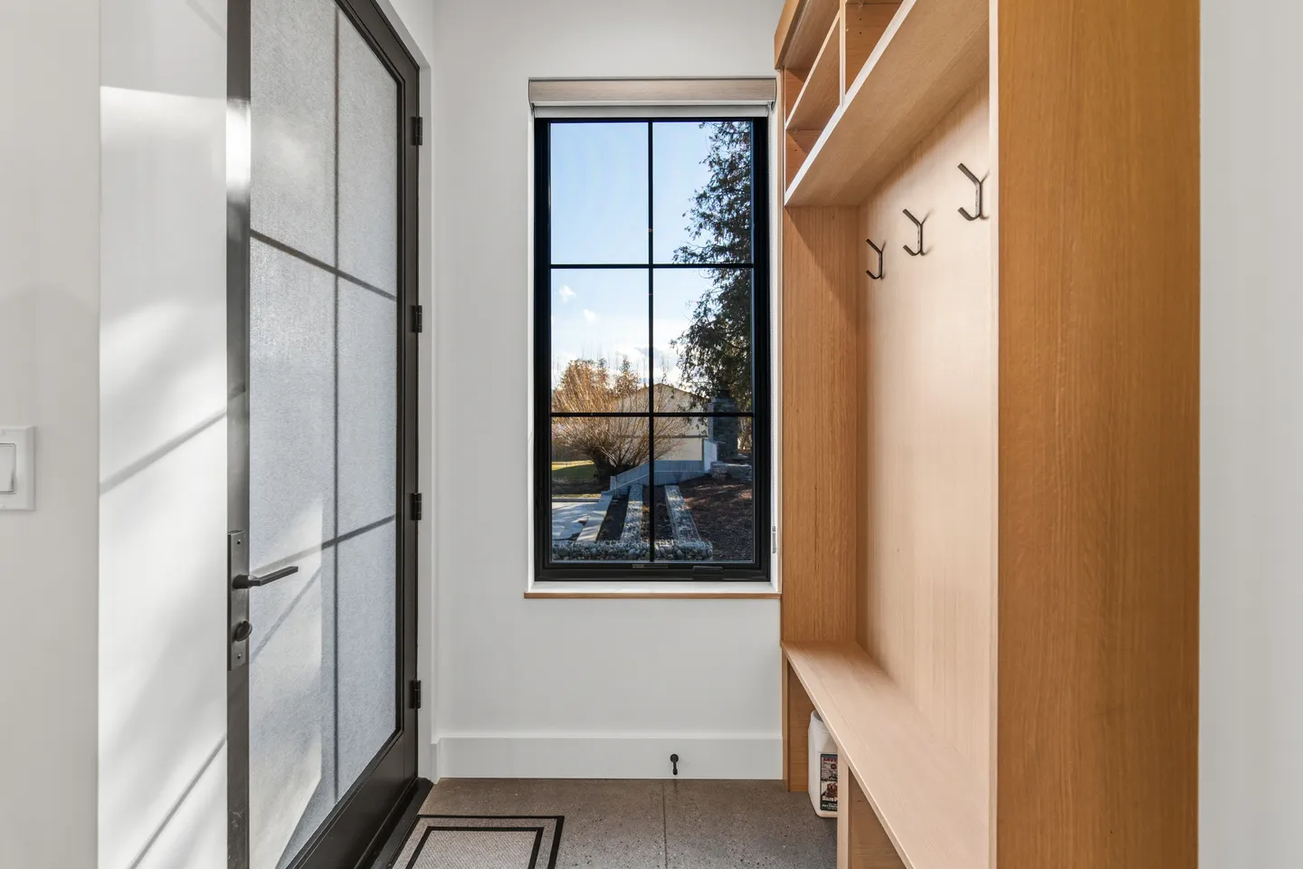 Mudroom entryway with a frosted glass door, a black-framed window overlooking the yard, and a wooden built-in bench with coat hooks.