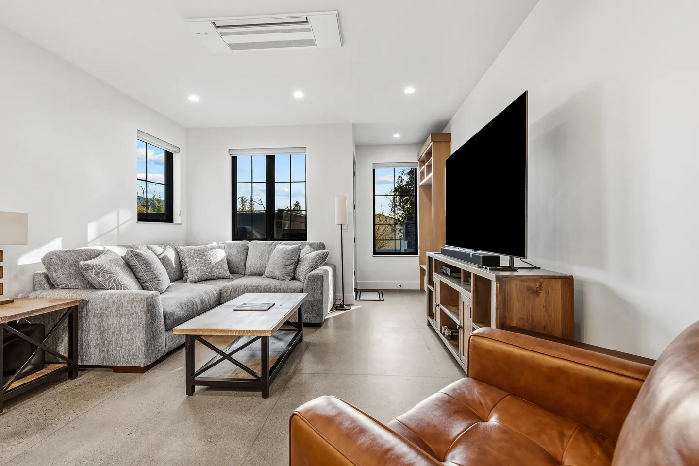 Living room with a large gray sectional sofa, coffee table, leather armchair, and mounted flat-screen TV on a wooden media console.