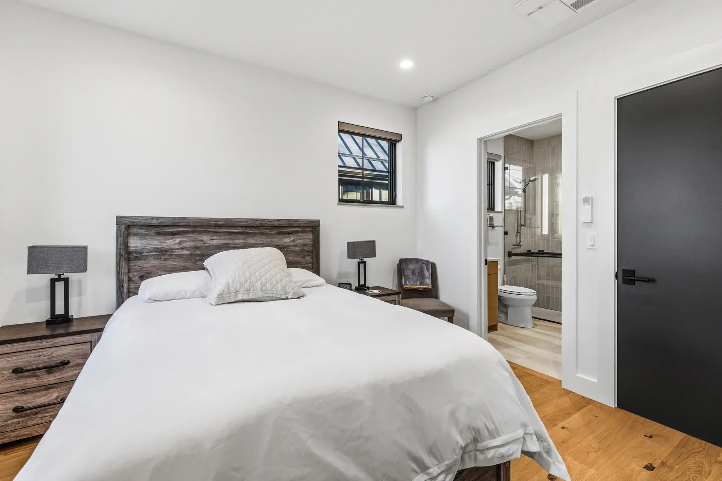 Bedroom with a wooden headboard, white bedding, nightstands, and an open doorway leading to an en-suite bathroom.
