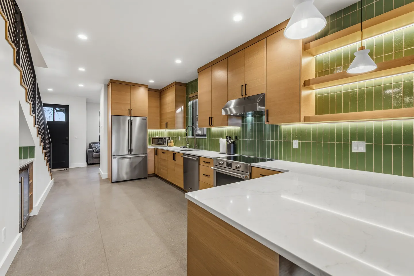 Modern kitchen with light wood cabinetry, green vertical tile backsplash, stainless steel appliances, and white countertops.