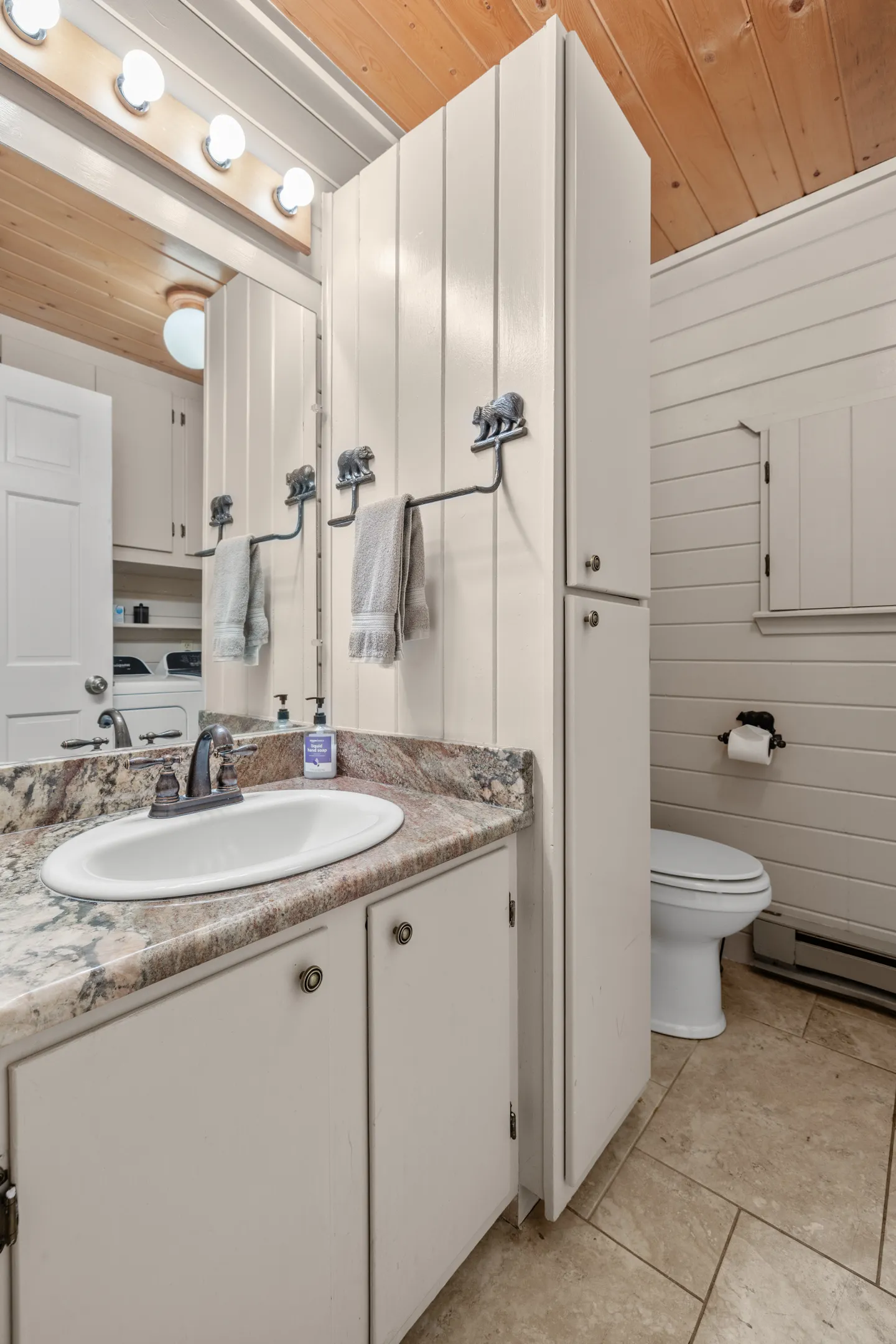 Bathroom with white vanity, speckled countertop, tall white cabinet, and a toilet next to horizontal paneled walls.