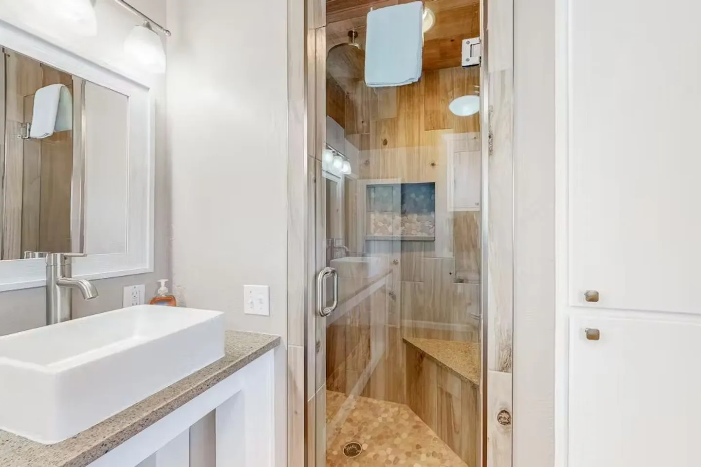 Bathroom featuring a vessel sink on a vanity and a glass-enclosed walk-in shower with wood-look tile and a corner bench.
