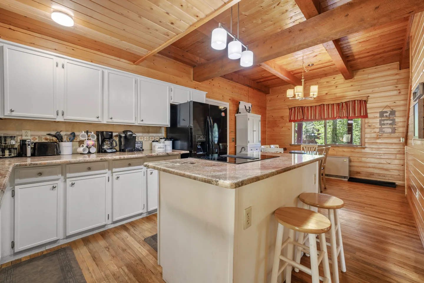 Kitchen with white cabinetry, an island with barstools, wood-paneled walls, and a beamed wooden ceiling.