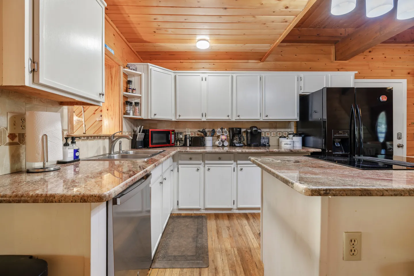 Kitchen with white cabinetry, granite countertops, a wood-paneled ceiling, and black appliances.
