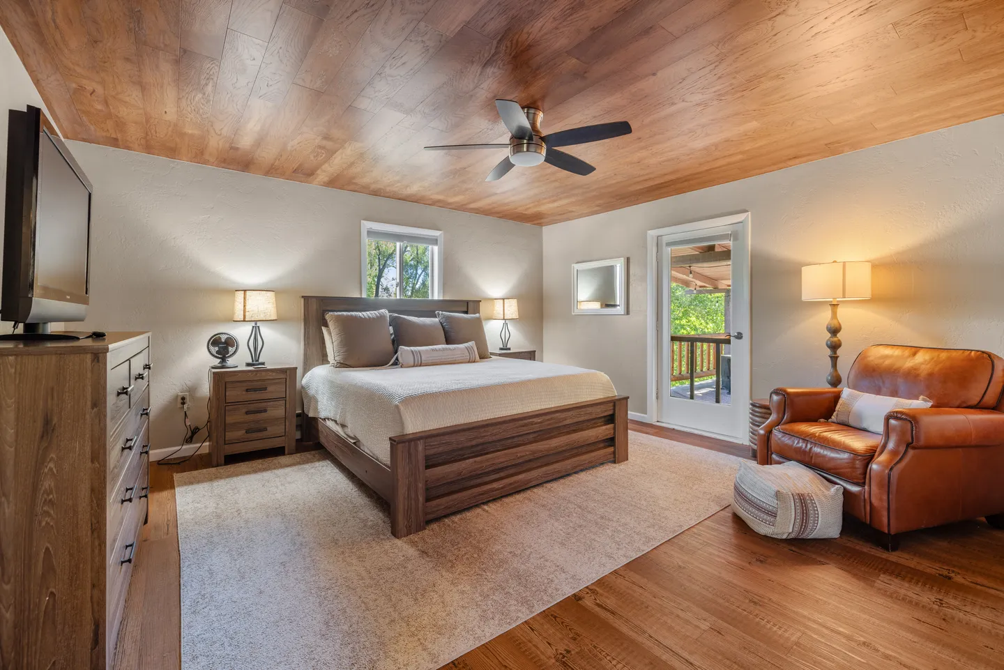Bedroom featuring a wooden bed, ceiling fan, wood-plank ceiling, leather armchair, and an exterior door leading to a balcony.