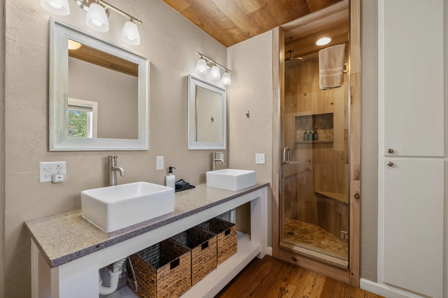 Bathroom with double vessel sinks, wood ceiling, framed mirrors, and glass-enclosed walk-in shower.