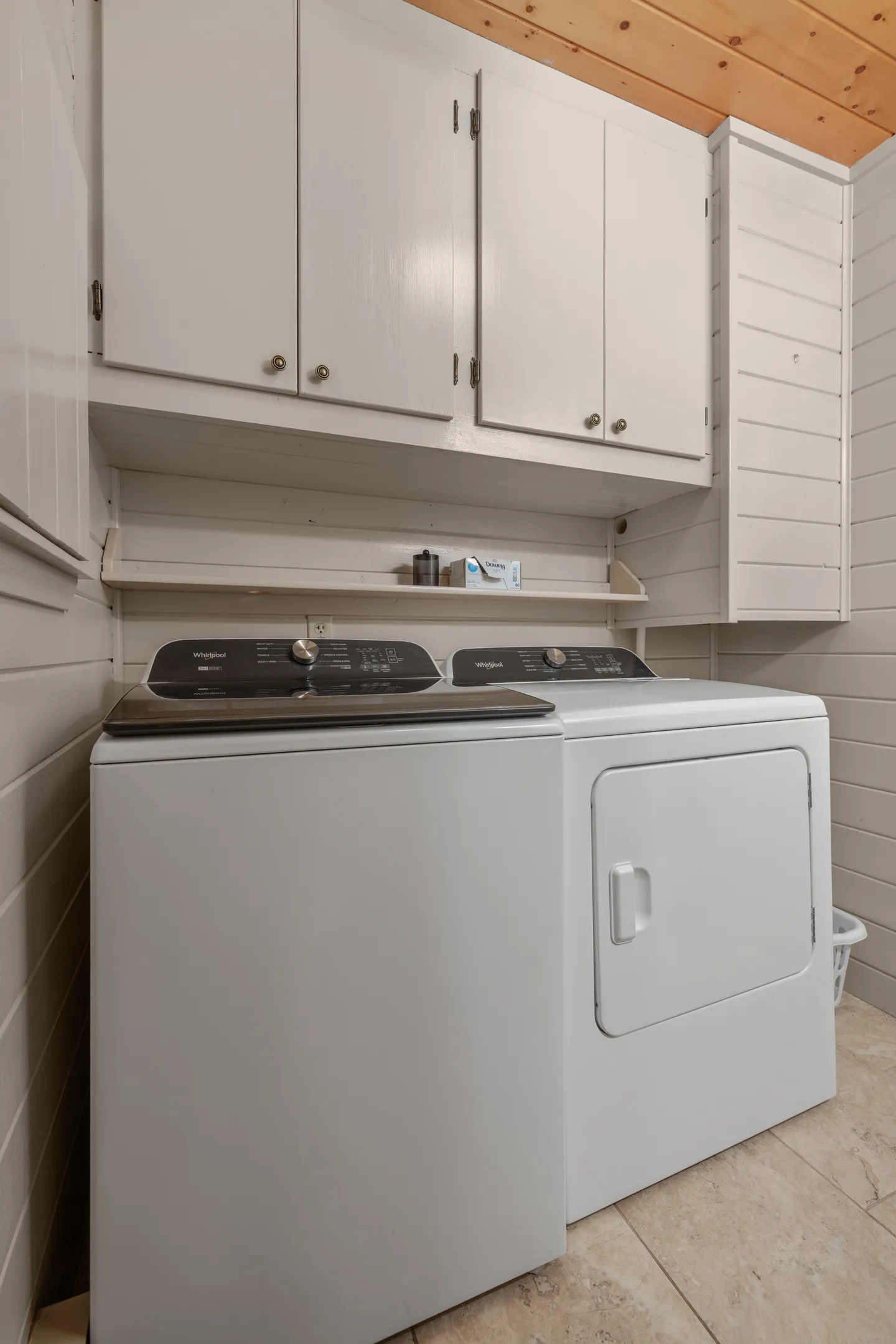 A laundry room area with a white top-load washer, a front-load dryer, and white wall-mounted cabinets above.
