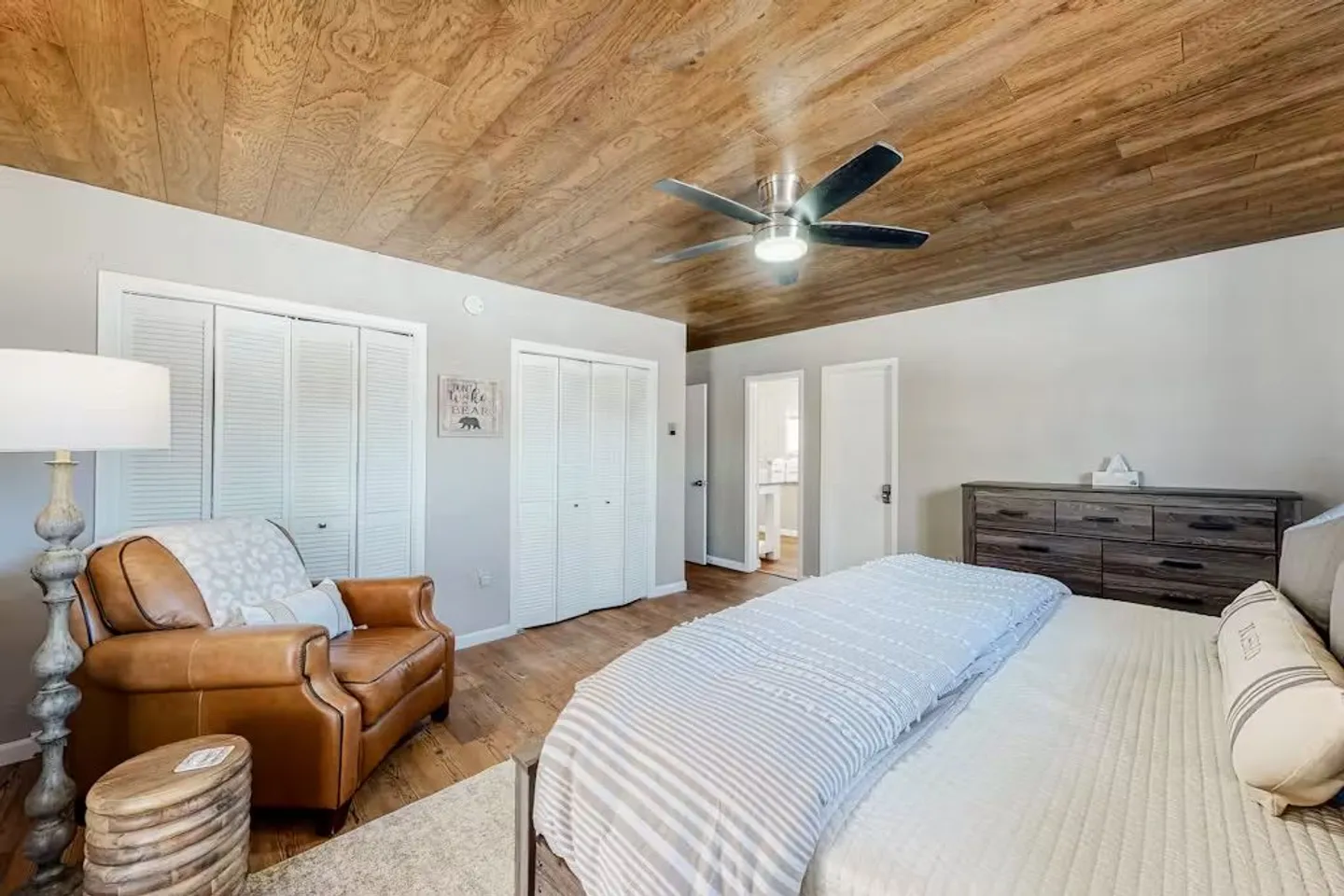 Bedroom featuring wood-paneled ceiling, a bed with striped bedding, a leather armchair, and a dresser.