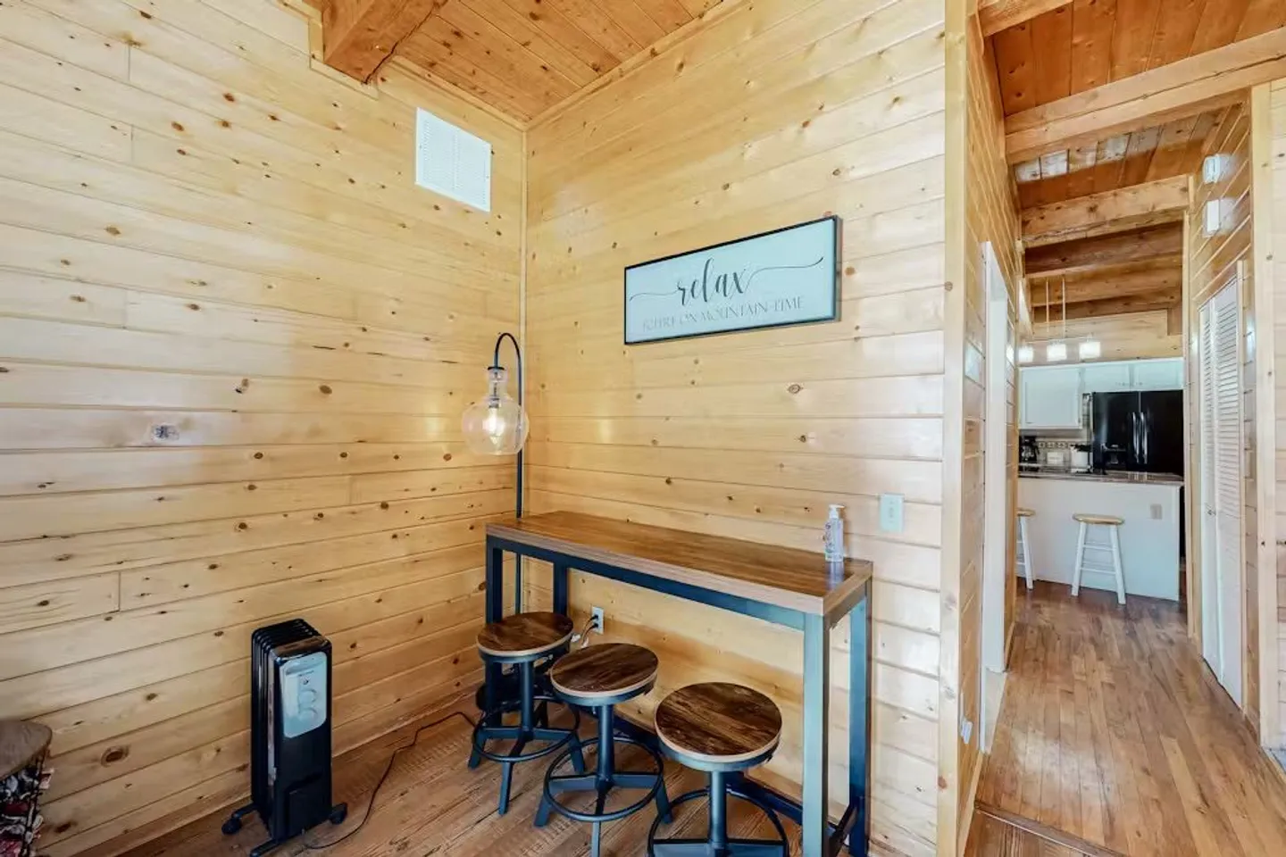 A small dining or workspace nook with wood-paneled walls, featuring a high-top table and three round barstools.