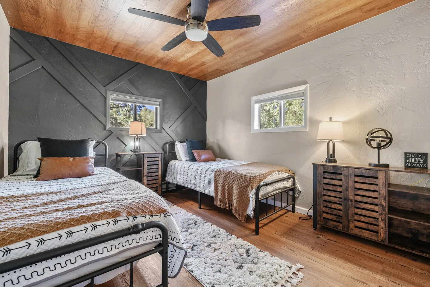 Bedroom featuring two twin beds with black metal frames, a dark geometric accent wall, and a wood plank ceiling with a ceiling fan.